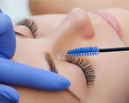 Esthetician brushing eyelash extensions or lash lift and tint.